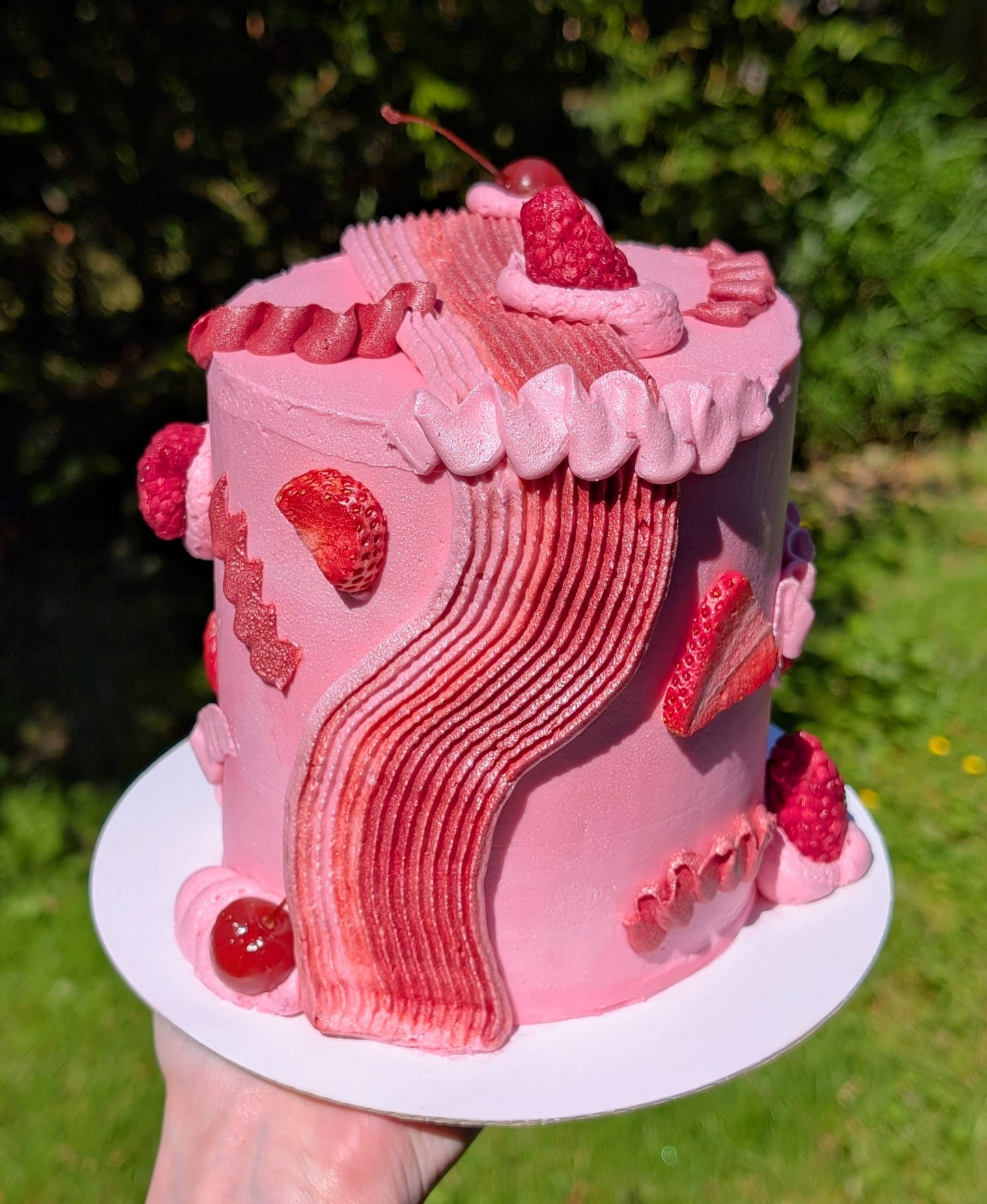 Pink hand-decorated celebration cake with cherries and berries
